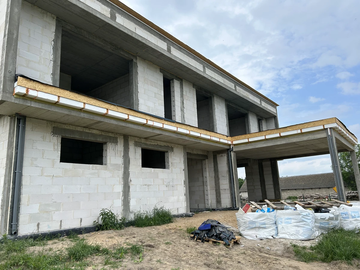 Surowy budynek z bloczków betonowych, bez pokrycia dachowego i z workami materiałów budowlanych na parceli