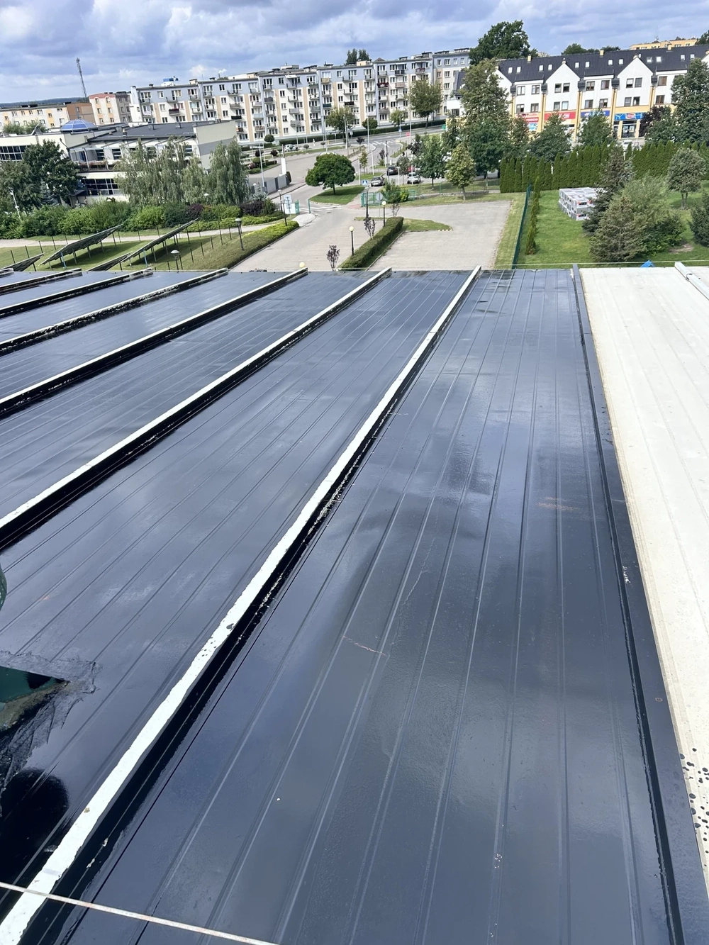 Montaż czarnej blachy trapezowej na stropodachu z widokiem osiedla w tle
